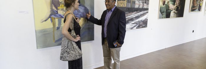 La ganadora del premio del año pasado conversa con uno de los organizadores en la exposición de las obras